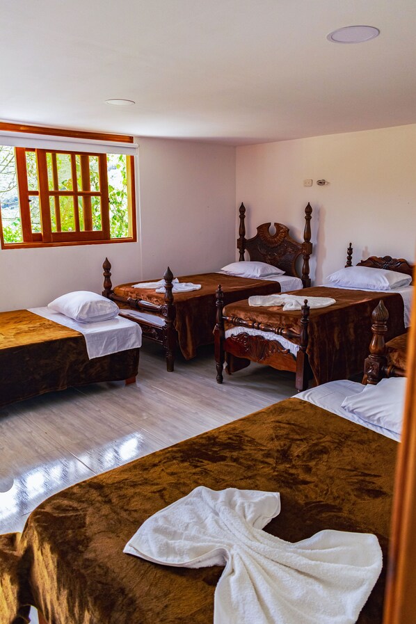 A hotel room with four wooden beds, a wooden table, and a window with a view of greenery.