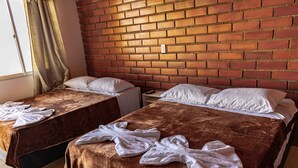 Twee eenpersoonsbedden met bruine dekens en witte kussens, een bakstenen muur en een raam met gordijnen.