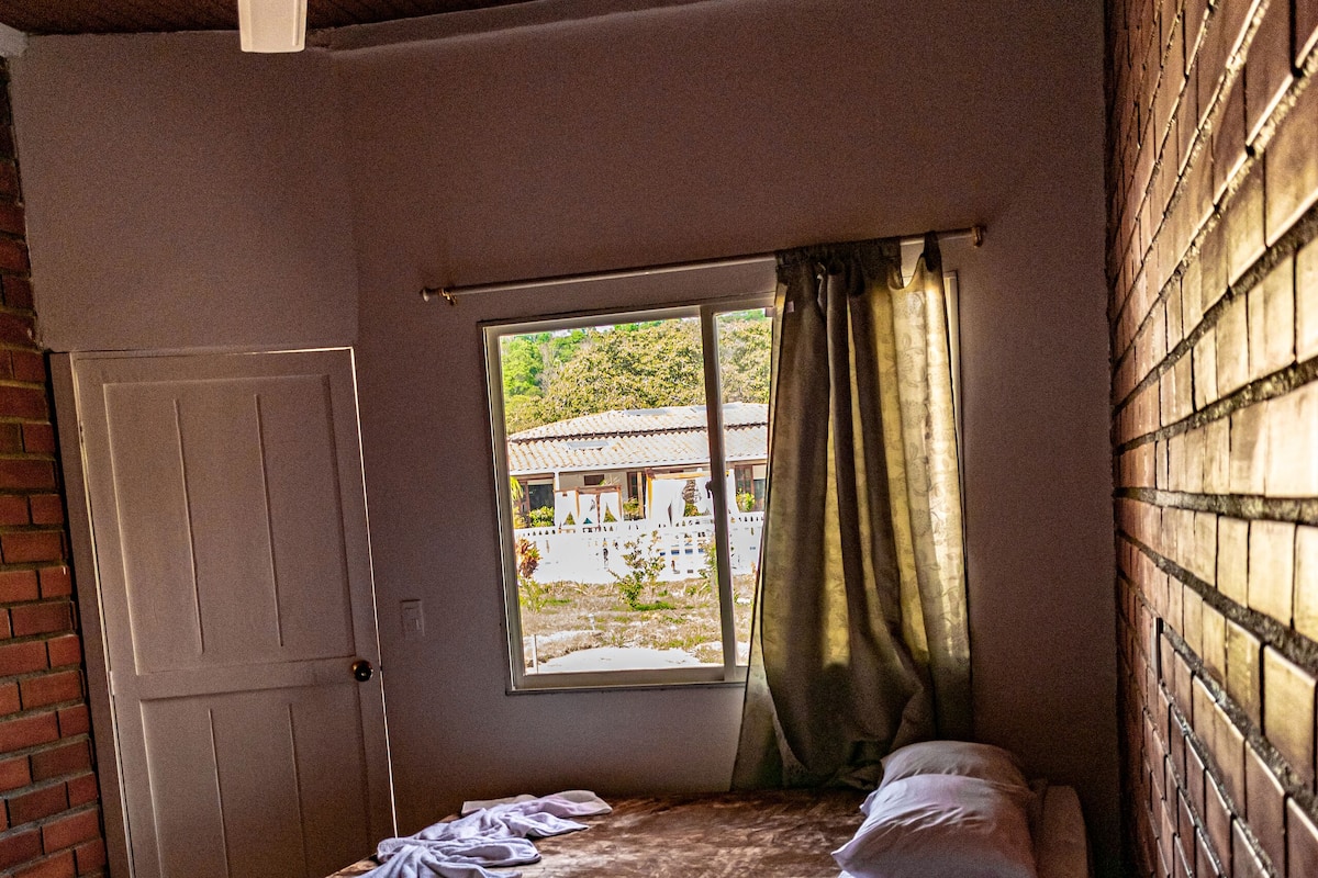 Een kamer met twee bedden, een raam met gordijnen, een deur en een bakstenen muur.