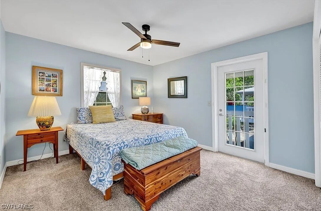 A bedroom with a bed, two bedside tables, a ceiling fan, and a view of the outside through a door.