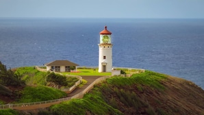 Un faro con techo rojo, un edificio pequeño adyacente y un camino que lleva al faro.