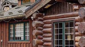 Une cabane en rondins avec un banc en bois à l’extérieur, une cheminée et une fenêtre à carreaux.