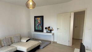 Un salon moderne avec un canapé beige, une table basse blanche, une petite table blanche et un tableau accroché au mur.