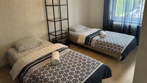 Deux lits simples avec une literie à motifs, une grande étagère noire et une fenêtre avec des rideaux.