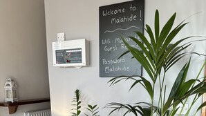 A modern room with a wooden table, potted plants, a blackboard with welcome message, and a thermostat. - Malahide Guest Rooms (Malahide)