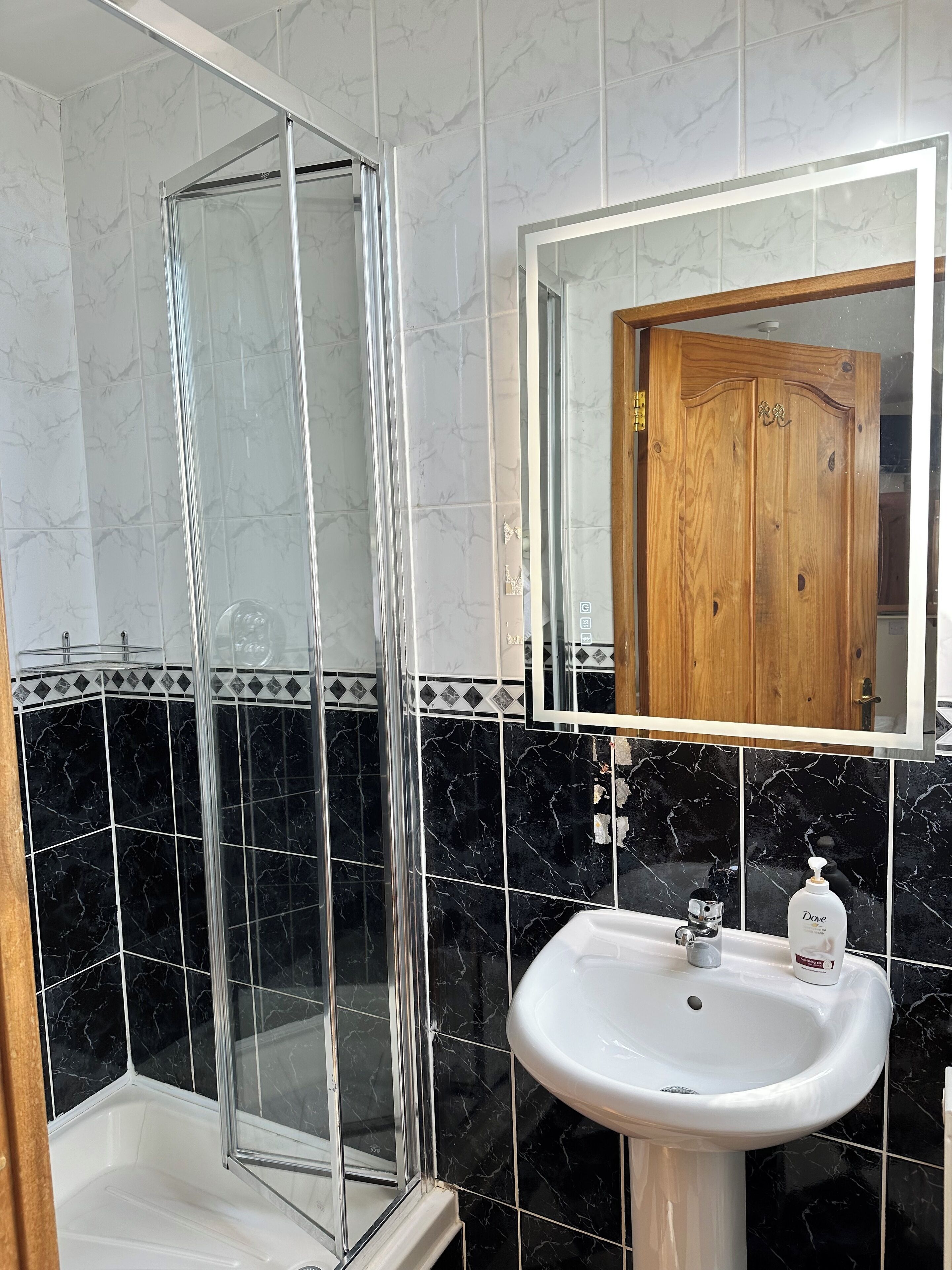 Un baño con cabina de ducha de vidrio, un lavamanos blanco y baldosas de mármol negro.