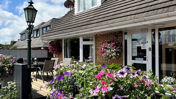 A house with a covered patio, outdoor seating, and a variety of flowers. - Malahide Guest Rooms (Malahide)