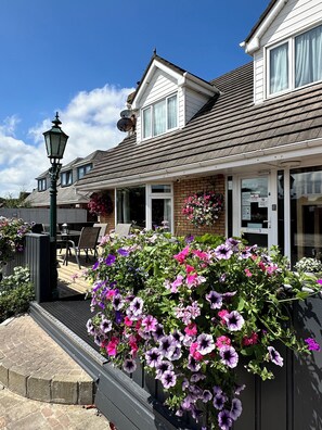 A house with a covered patio, outdoor seating, and a variety of flowers. - Malahide Guest Rooms (Malahide)