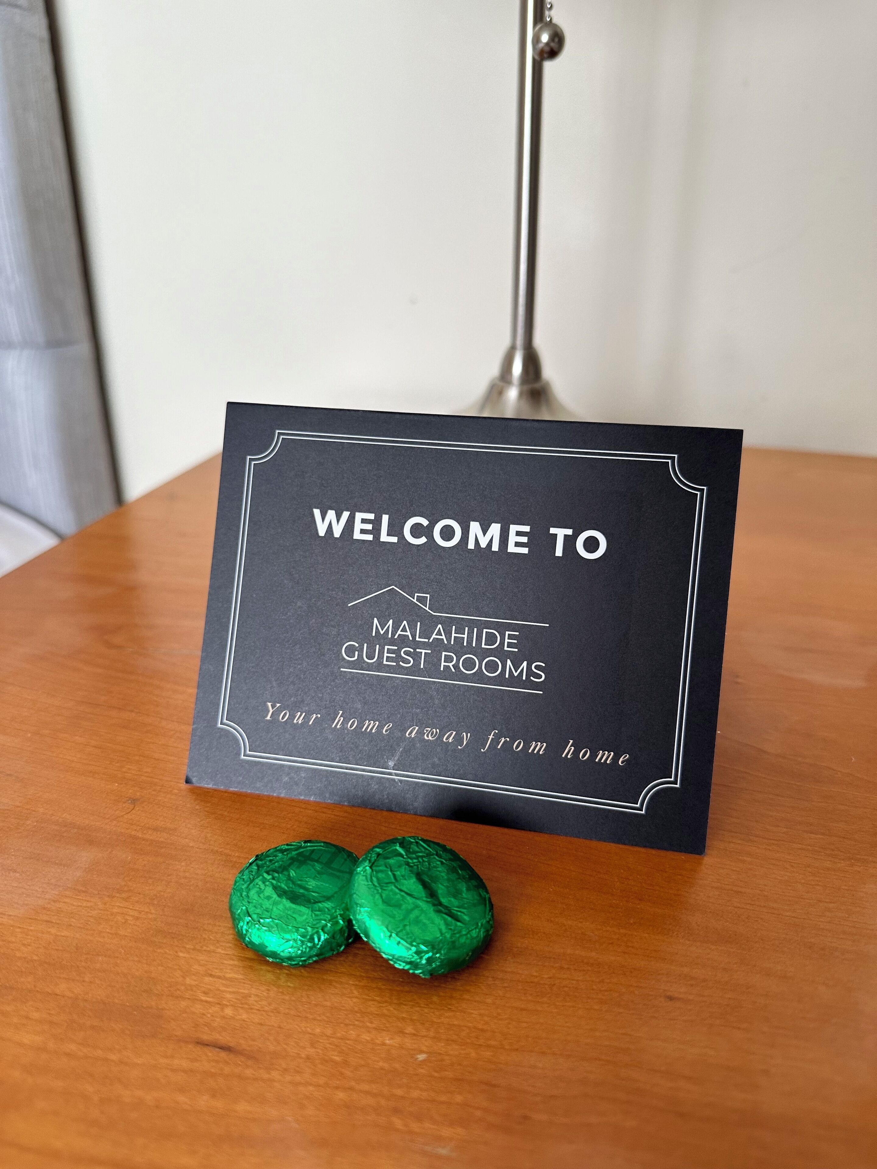A sign with "WELCOME TO MALAHIDE GUEST ROOMS" and "Your home away from home" on a wooden table.