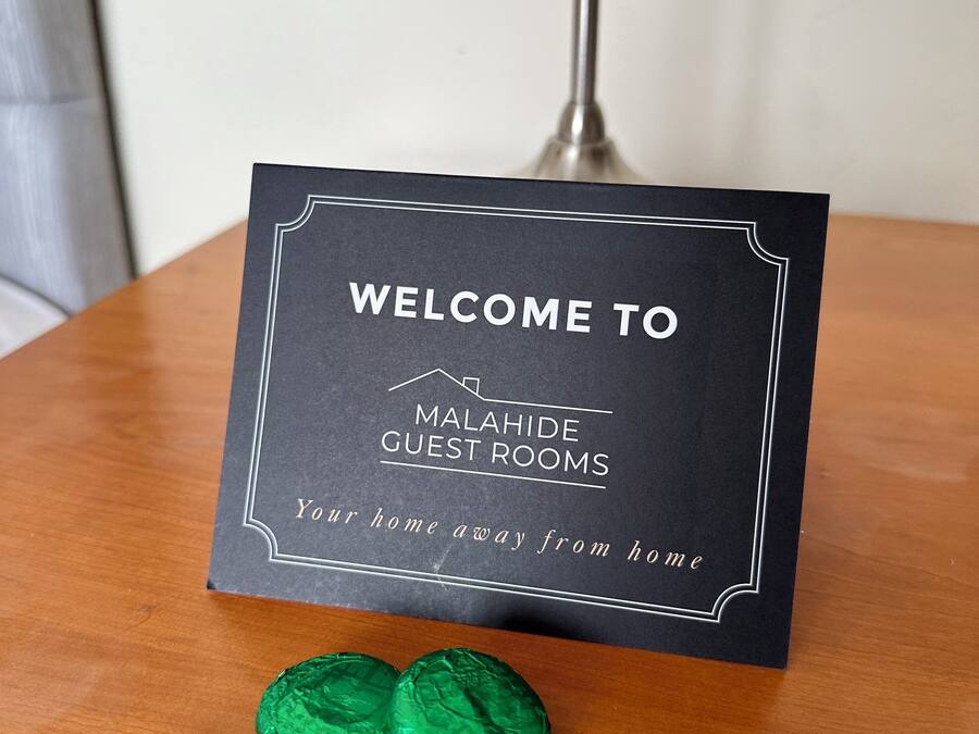 A sign with "WELCOME TO MALAHIDE GUEST ROOMS" and "Your home away from home" on a wooden table.