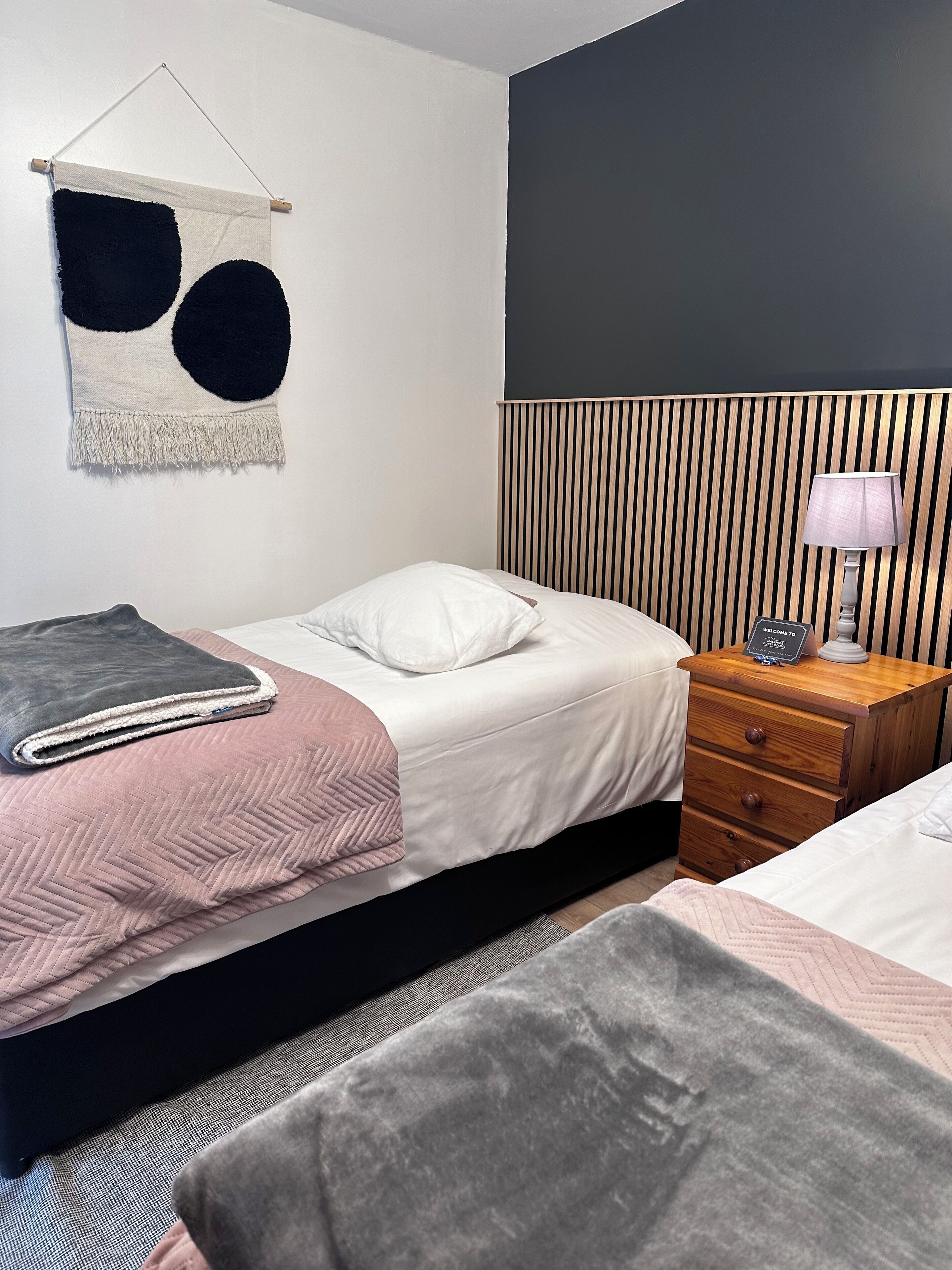 A bedroom with a bed, bedside table, lamp, and a wall-mounted tapestry.