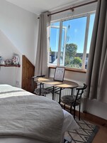 Un dormitorio con cama, una mesita con sillas, una ventana con cortinas y un cartel de bienvenida.