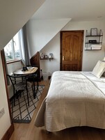 Un dormitorio con una cama grande, una puerta de madera, una mesita con una silla y una ventana con cortinas.