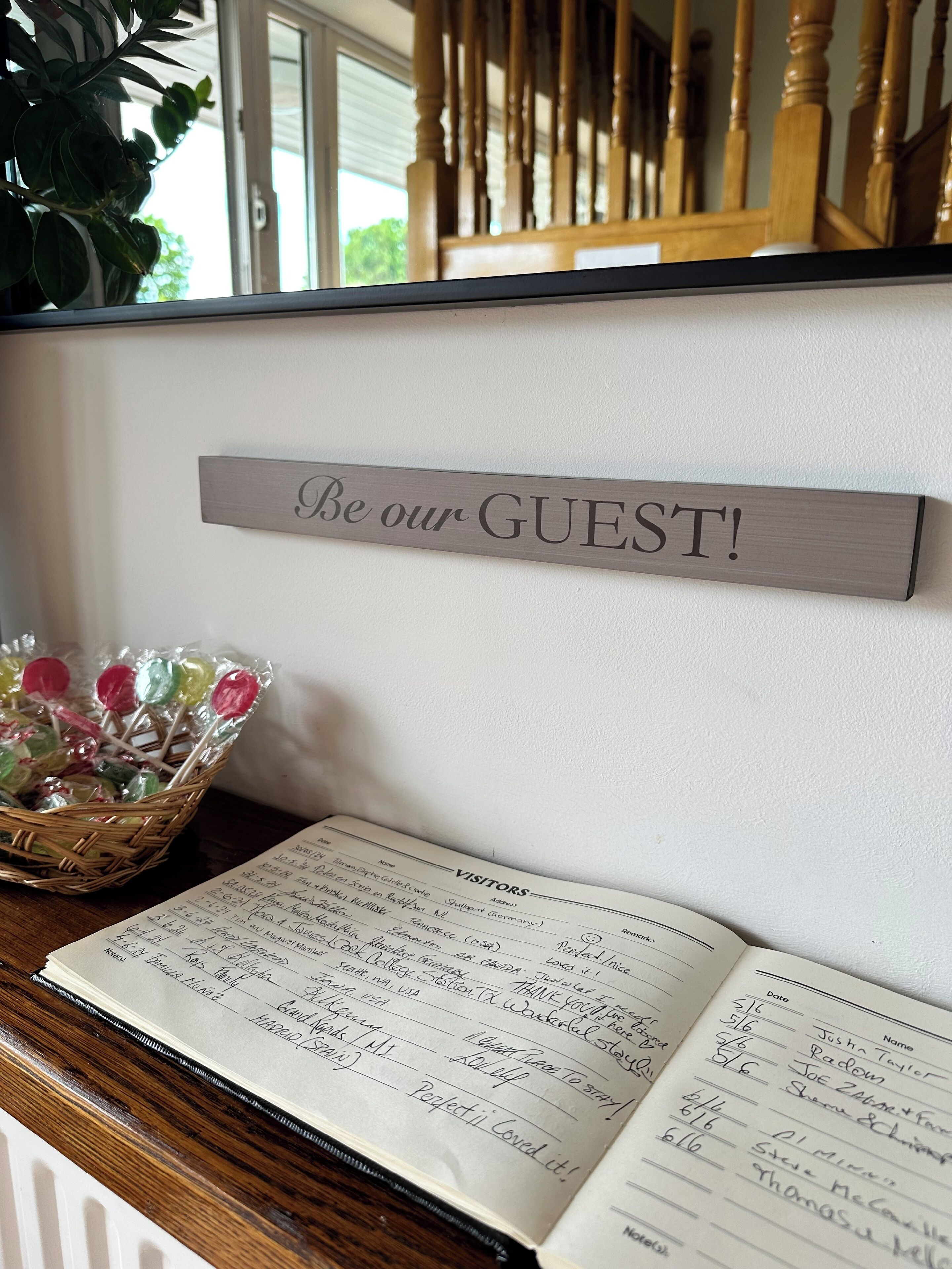 A sign that reads "Be our GUEST!" above a guest book on a wooden table.