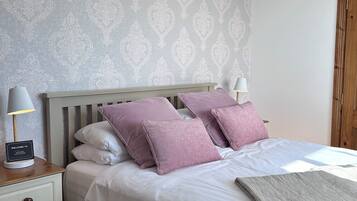 A neatly made bed with white and purple bedding, a bedside table with a lamp, and a welcome sign.