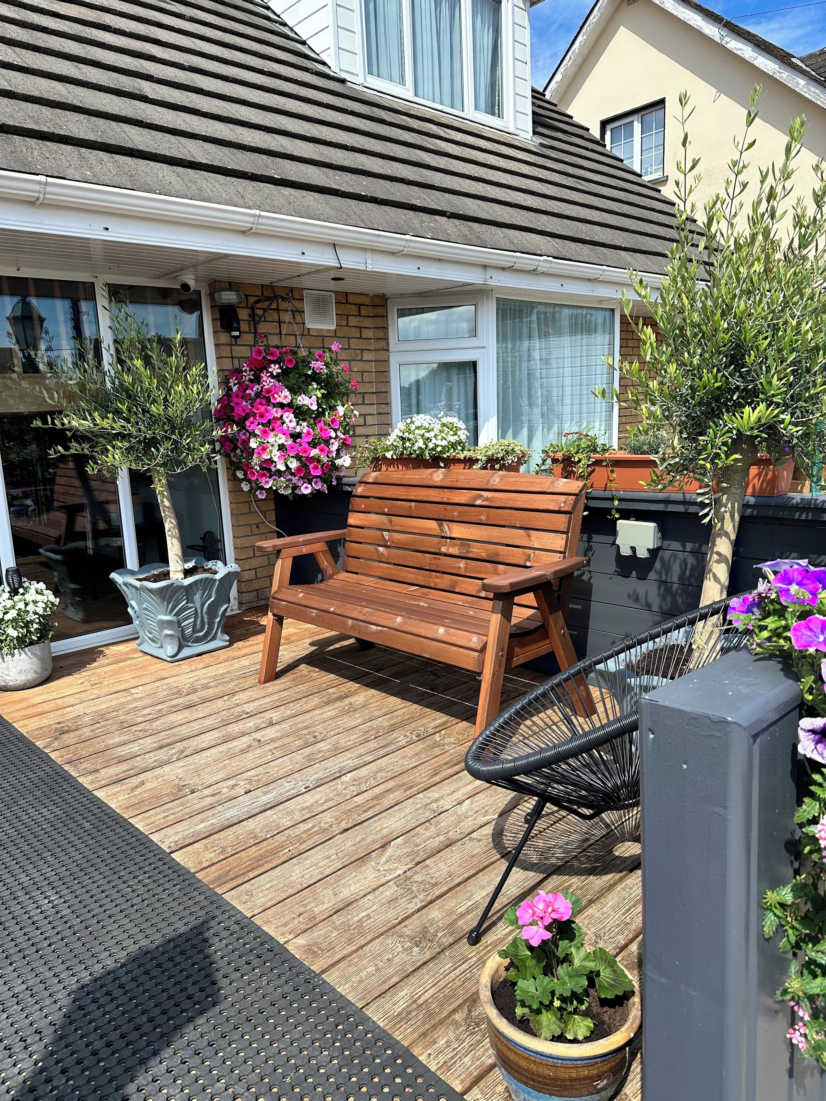 Une terrasse en bois avec un banc, des plantes en pot, une chaise et une petite table.