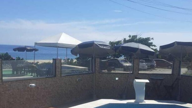 Piscina con vista al océano, rodeada de sombrillas y un muro de piedra.
