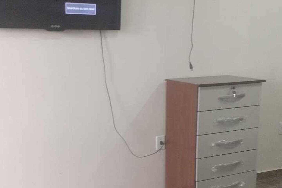 A room with a bed, a TV mounted on the wall, a fan, and a wooden cabinet.