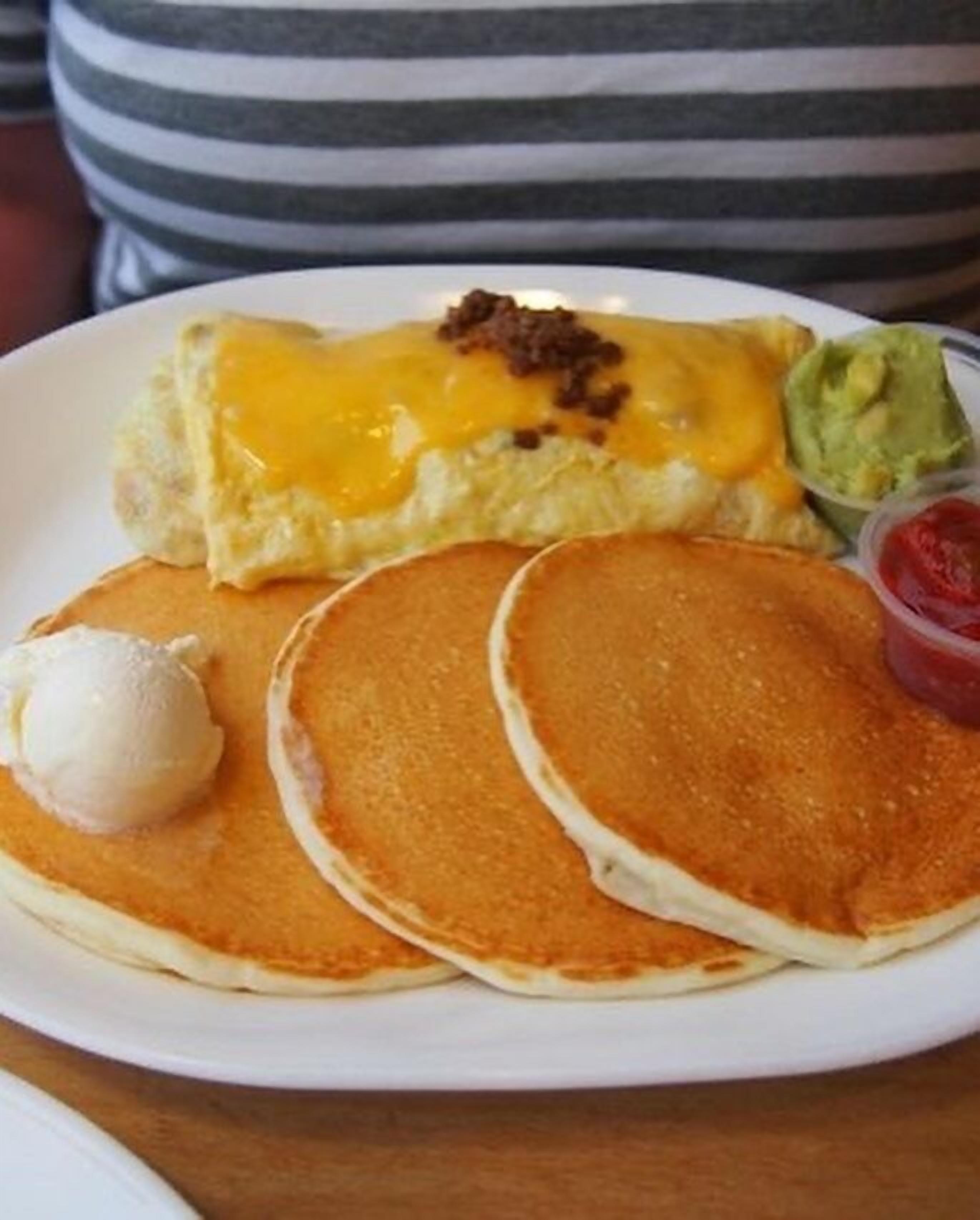 A plate with pancakes, a piece of toast with cheese and bacon, a scoop of ice cream, and a small container of ketchup.