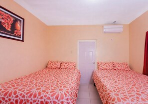 Una habitación con dos camas, una puerta, un equipo de aire acondicionado y un cuadro en la pared.