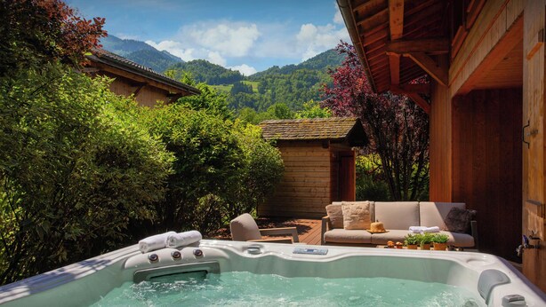 Una vasca idromassaggio con un patio in legno, immersa nel verde e con le montagne sullo sfondo.