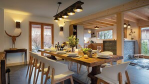 Zona pranzo con tavolo in legno apparecchiata per sei persone, circondata da sedie bianche.
