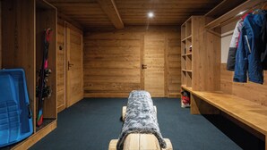 Eine Holzhütte mit Schlafbereich, ausgestattet mit einem Holzbett, einer Bank sowie einer weiteren Bank mit Skiern und einer Tasche.