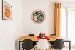 A dining area with a wooden table, black and white chairs, a red placemat, a bottle, and a bowl of fruit.