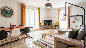 A modern living room with a dining area, a sofa set, a TV, and a large window with curtains. - Happy Stay Disneyland Paris - Garden Apartment + Parking (Montévrain)