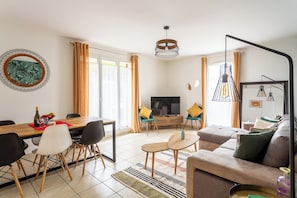 A modern living room with a dining area, a sofa set, a TV, and a large window with curtains.