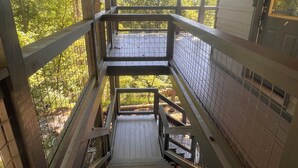 Eine Holztretppe mit Metallgeländern führt zu einer überdachten Terrasse mit Blick auf Bäume.