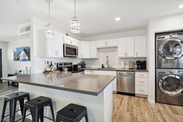 A modern kitchen with white cabinets, stainless steel appliances, a central island with stools, and pendant lighting.