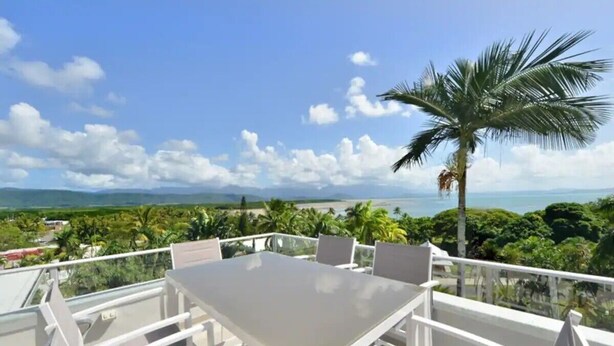 A balcony with a table and chairs overlooking a scenic view of the ocean and greenery. - Centrally located ground floor of 2 storey Artist's modern studio house. (Port Douglas)