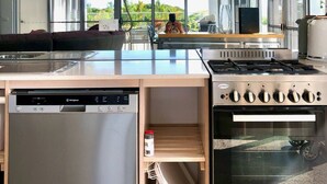A modern kitchen with a built-in dishwasher, a stainless steel stove, and a microwave above the counter. - Centrally located ground floor of 2 storey Artist's modern studio house. (Port Douglas)
