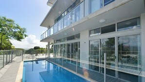 A modern hotel with a glass-enclosed infinity pool, a wooden deck, and a view of the surrounding landscape. - Centrally located ground floor of 2 storey Artist's modern studio house. (Port Douglas)