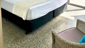 A hotel room with a large bed, a wicker chair, and a view of a pool through a glass door. - Centrally located ground floor of 2 storey Artist's modern studio house. (Port Douglas)