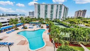 A hotel with a swimming pool, palm trees, and a large building in the background. - Amazing Condo 3 min to the Beach (Sunny Isles Beach)