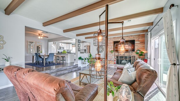 A spacious living area with leather sofas, a coffee table, and a hanging light fixture. There is a kitchen in the background with a brick wall and a dining area with chairs. - Walkable Chula Vista Home w/ Covered Patio (Chula Vista)