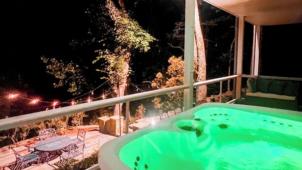A hot tub with a green light, outdoor seating area, and a view of trees at night.