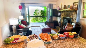 A spacious living room with a large dining table set for a meal, a fireplace, and a balcony with a view of greenery.
