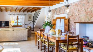 A spacious living room with a wooden ceiling, a dining area with a wooden table and chairs, a sofa, and a television. - Beautiful house with views to the mountains near Pollensa (Pollensa / Pollença)