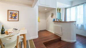 Een moderne keuken met witte kastjes, een eethoek met een tafel en stoelen, en een stadszicht door grote ramen.