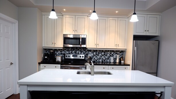 A modern kitchen with white cabinetry, stainless steel appliances, and pendant lighting.