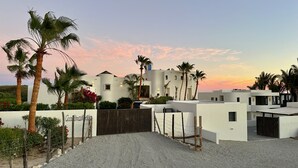 A modern villa with a white exterior, surrounded by palm trees and a gravel driveway. - Exquisite oceanfront luxury casa, Pezula Beach (San Jose del Cabo)