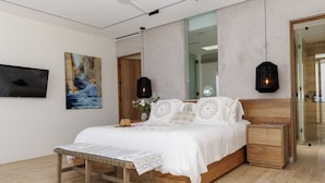 A modern bedroom with a wooden bed, a bedside table, a bench, and artwork on the walls. - Exquisite oceanfront luxury casa, Pezula Beach (San Jose del Cabo)