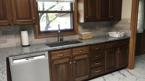 A kitchen with wooden cabinets, a Bosch dishwasher, a window with a view, and a marble floor.