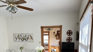 A dining area with a wooden table, chairs, a bench, a TV, and a ceiling fan.