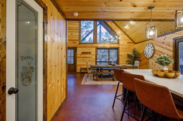 A wooden interior with a dining area, a clock, and a pantry door.