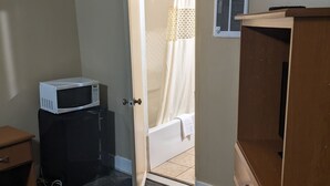 A bedroom with a bed, a wooden dresser, a microwave, and a bathroom visible through an open door. - Rainbow Motel (Hendersonville)