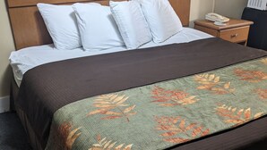 A neatly made bed with a brown quilt and a floral-patterned throw. - Rainbow Motel (Hendersonville)